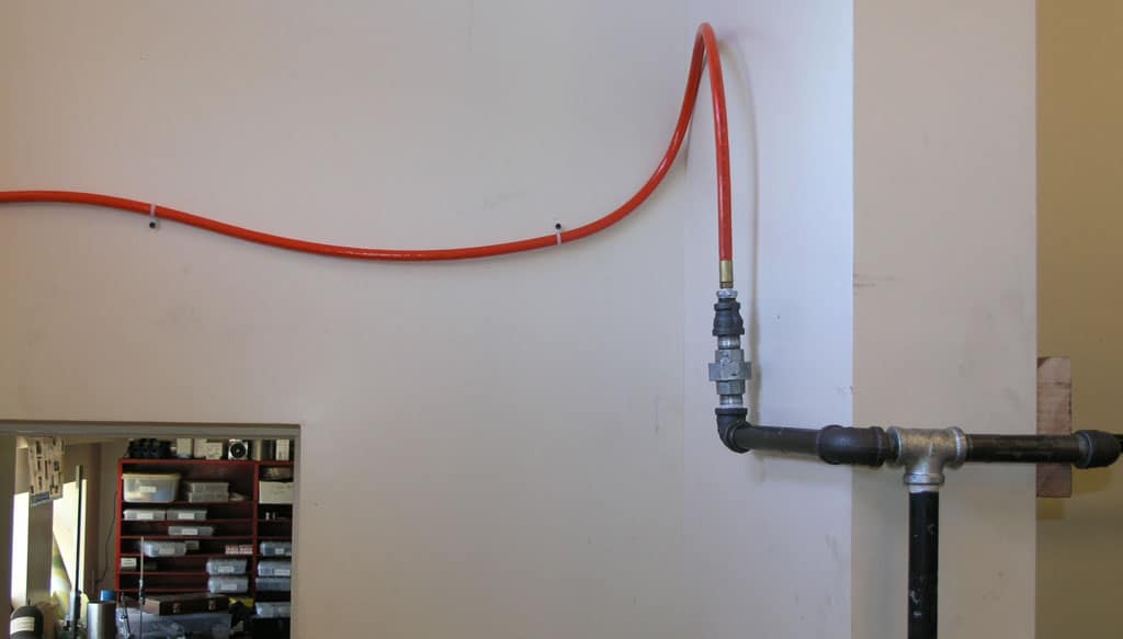 A red wall-mounted hose with fluid delivery system, likely used in machine shops or metrology environments.