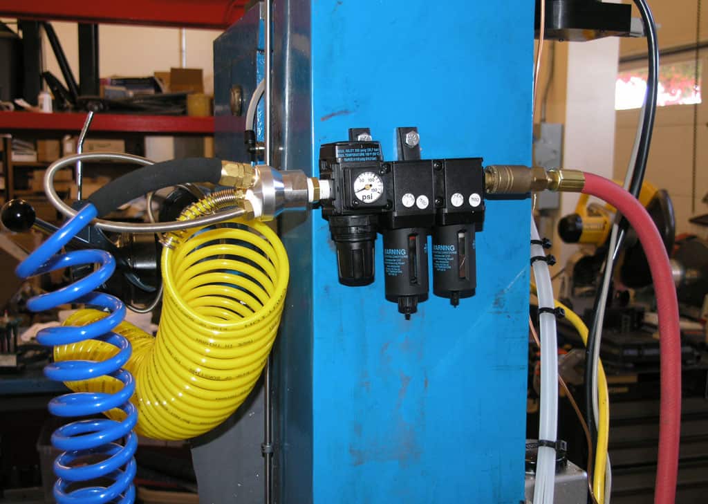 Air compressor system with gauges, valves, and regulators on blue metal frame.