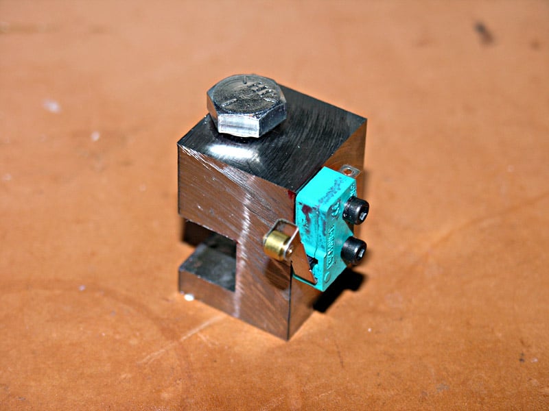 Metallic cube with teal electronic device attached, on brown surface in workshop setting.