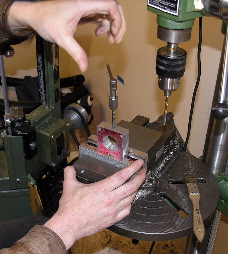 A person carefully operates a drill press in a workshop setting.
