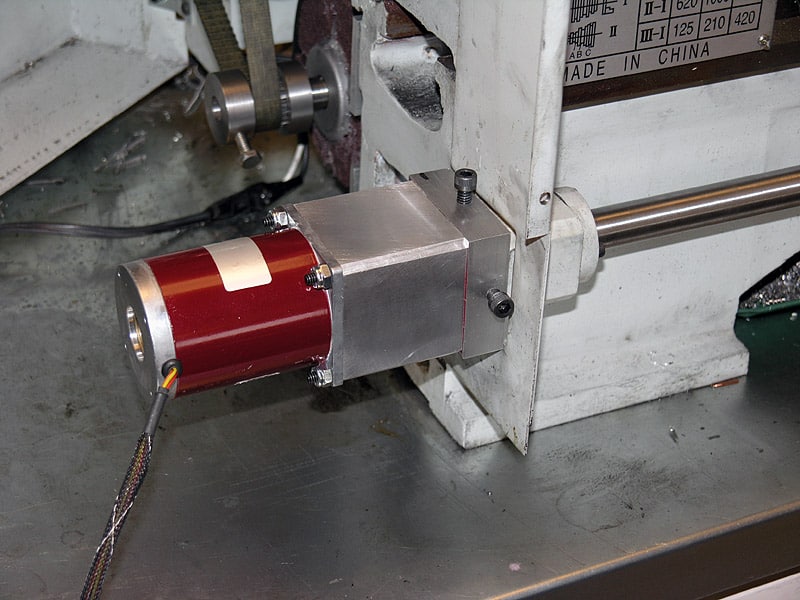 Metalworking lathe component with red cylindrical body, silver plate, bolts, screws, and wires.