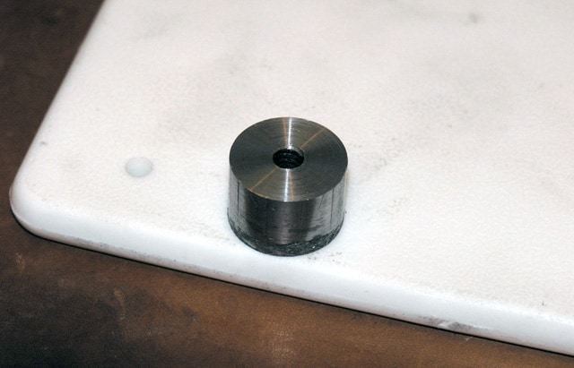 Cylindrical metal object with circular hole, resting on a white surface, smooth shiny finish.