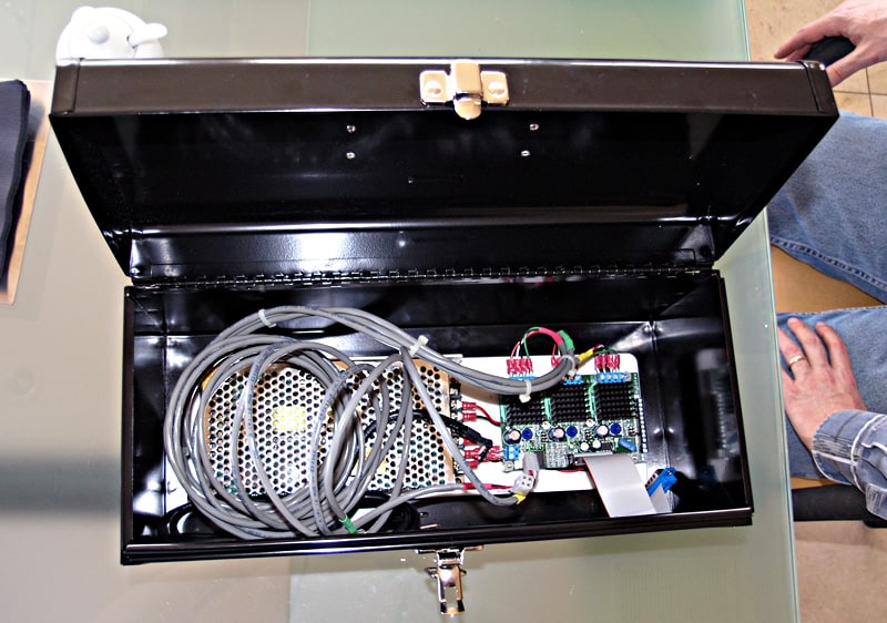 Black metal box with electronic components and circuit boards on a glass table.