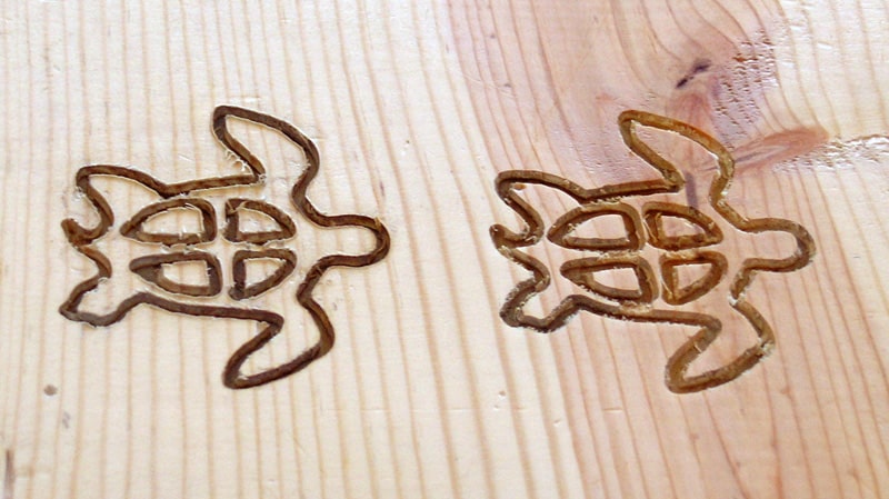 Two wooden boards with carved fish-like designs and symmetrical curved lines created using a router or engraving tool.