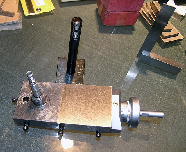 Metalworking vise with threaded rod on flat surface.