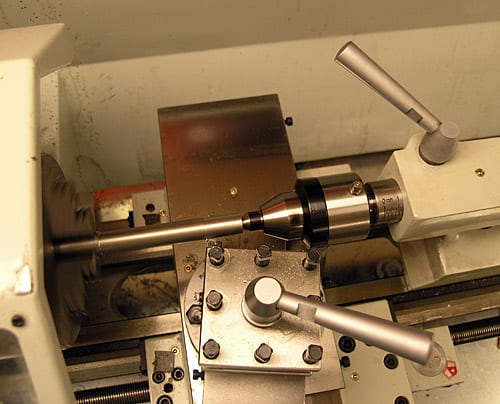 A lathe machine with a metal rod, silver handle, and metallic framework, featuring black knobs or bolts.