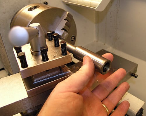 A person's hand holding a cylindrical object in front of a metal lathe or milling machine.
