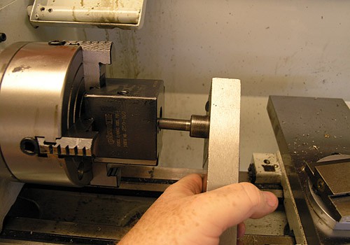 A person manually operates a milling machine with a hand-held tool producing sparks while cutting or shaping metal.