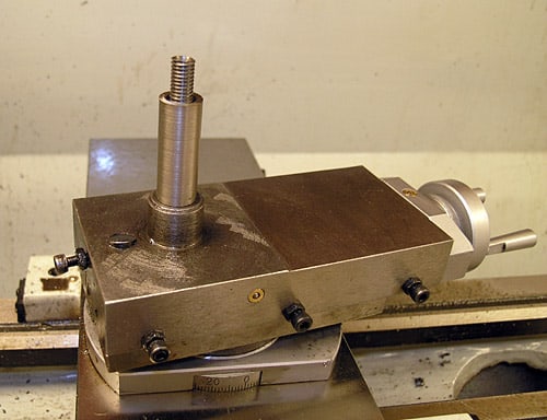 Metalworking machine tool with a square-shaped metal part attached, featuring a cylindrical protrusion on top.