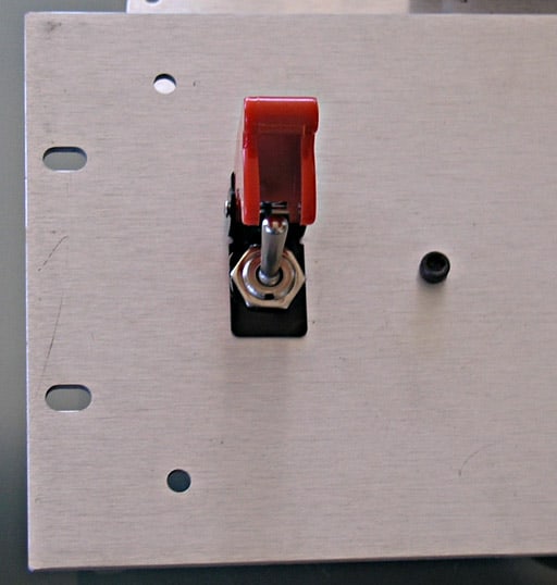 A close-up of a metal plate with a red toggle switch and black knob.