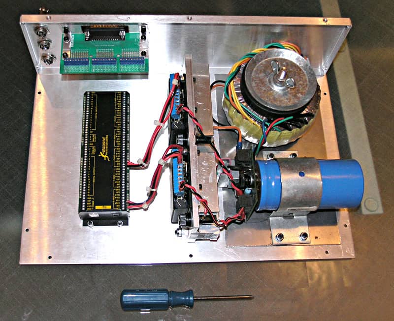 A silver metal box containing electronic components, a circuit board, motor, and blue cylinder.