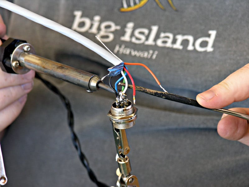 Hands holding wire stripper on gray t-shirt with Hawaii logo.
