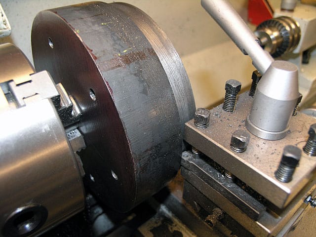 Metal lathe with cylindrical workpiece attached, featuring flat surface and small holes.