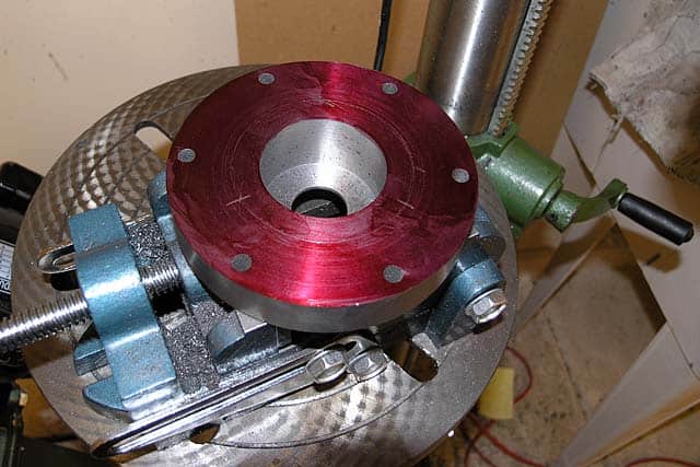 Metalworking vise with red anodized aluminum jaw on a metal table.