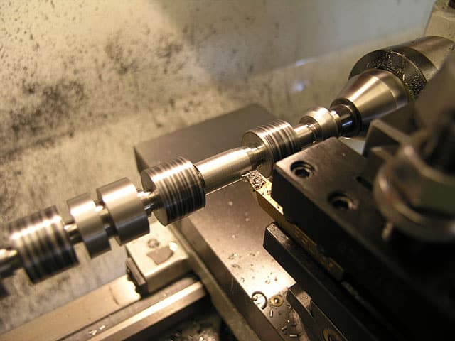 Metalworking lathe with cutting tool and two cylindrical workpieces.