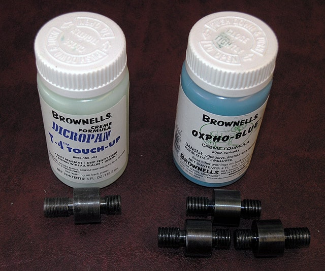 Two Brownells' Micropan and Oxpho-Blue chemical bottles with black cylindrical objects on a dark brown surface.