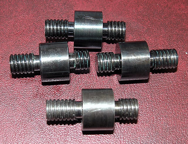 Five black metal threaded rods with cylindrical heads on a red leather surface.