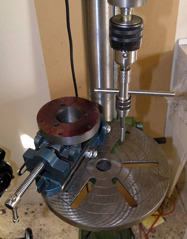 Metalworking drill press with vise on industrial workbench.