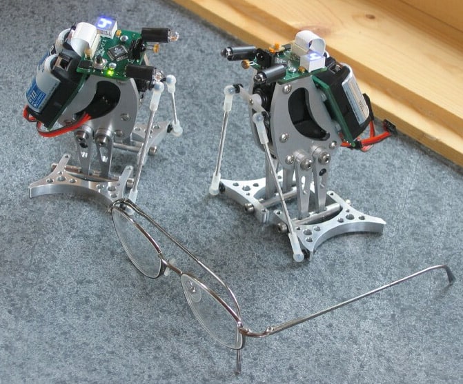 Two robotic penguin-like devices with metal bodies and various components on their heads on a gray workbench.