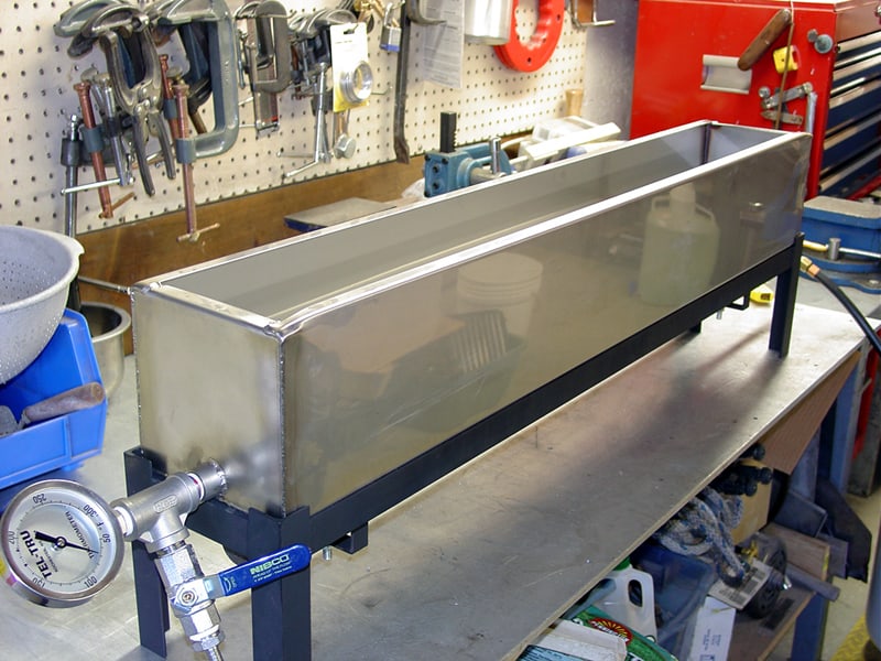 Stainless steel water tank on metal workbench with tools and equipment in a well-organized workshop.