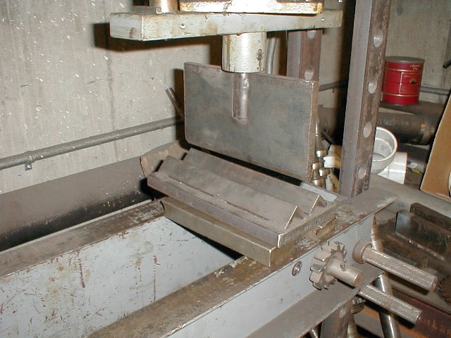 Industrial press or vise with worn metallic frame and open jaw.