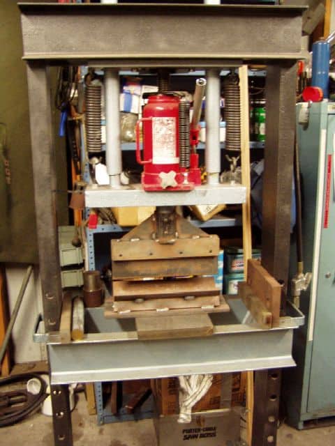 Heavy-duty press brake with red hydraulic cylinder, metal frame, and wooden clamps.