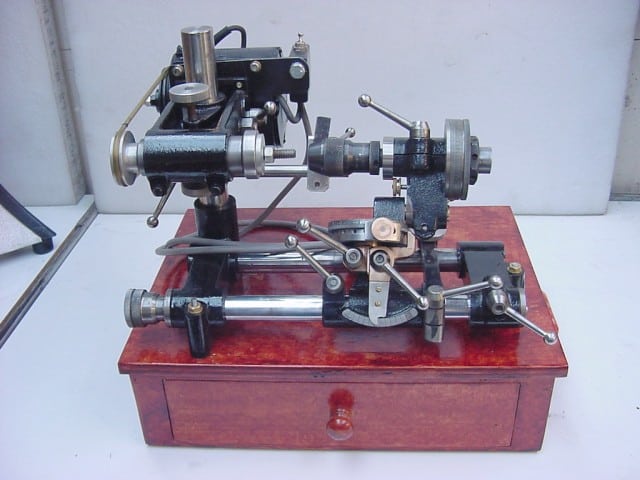 Vintage metal lathe with wooden base and rotating cutting tool.