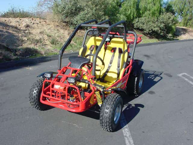 Red dune buggy with yellow seat and roll cage, on a dirt road or trail.