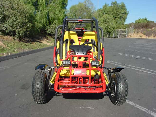 Red and yellow go-kart on asphalt road with black safety bars and off-road tires.