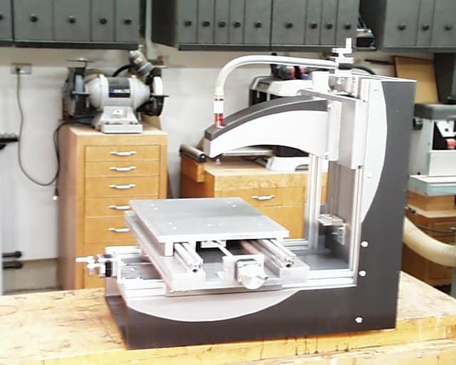 Large industrial metalworking machine with gray body and silver components on a wooden table in an industrial setting.