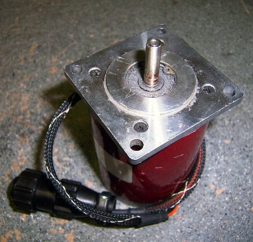 Red cylindrical stepper motor with black cord on dark gray surface.