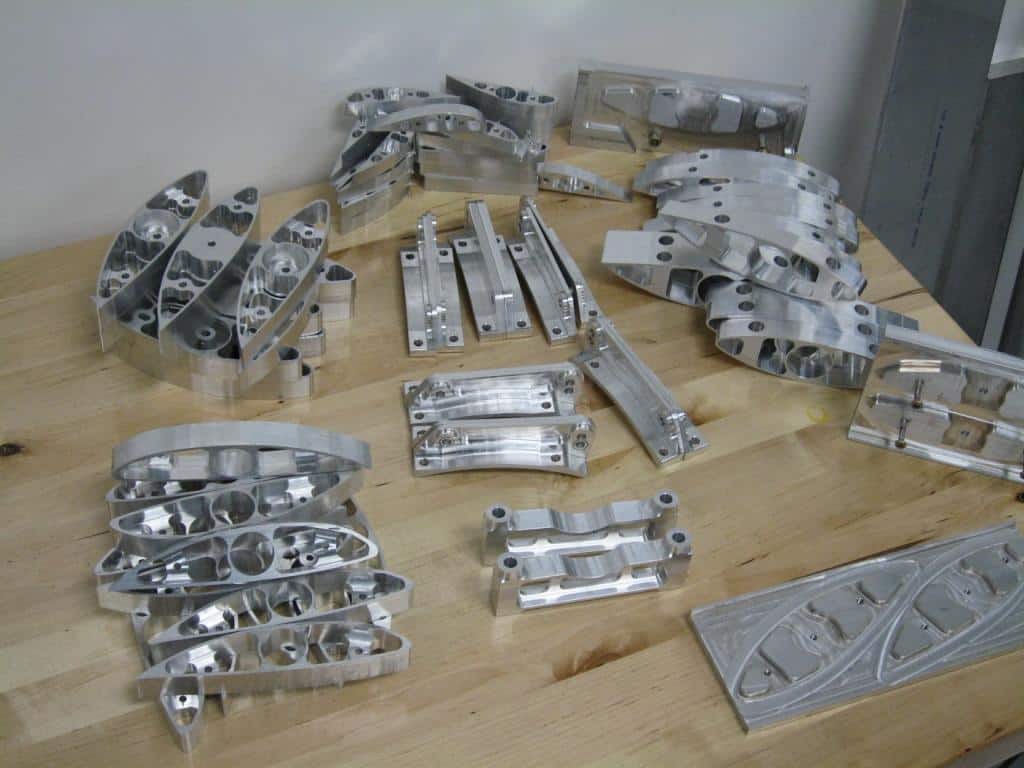Aluminum machined parts on wooden table in well-lit room.