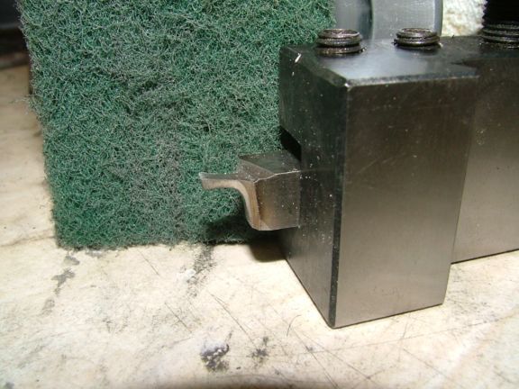Two metal pieces with screws sit atop a scratched white surface, behind a green scrubbing sponge.