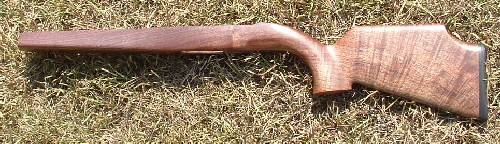 Wooden rifle stock on ground surrounded by dry grass.