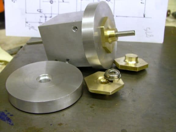 Metal parts, including a bearing cap, on a gray surface in a machine shop or manufacturing setting.