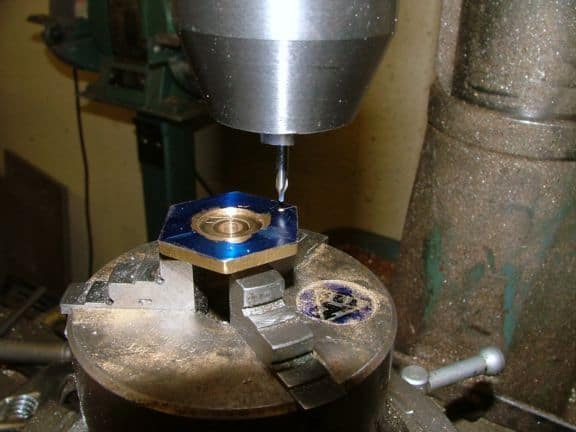 Metal object being drilled on a drill press in a machine shop.