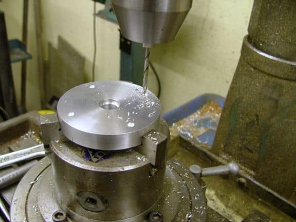 Stainless steel milling tool on industrial-grade drill press with metal cap in machine shop or fabrication facility.