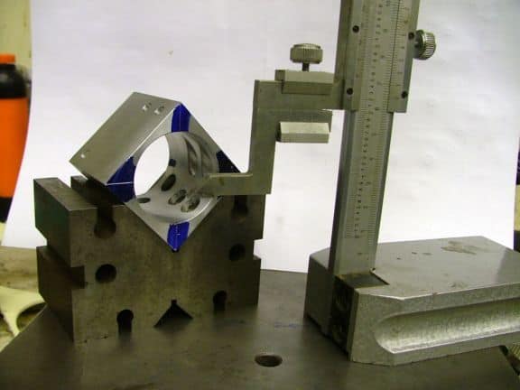 Metal part with blue accents being measured with precision tool.