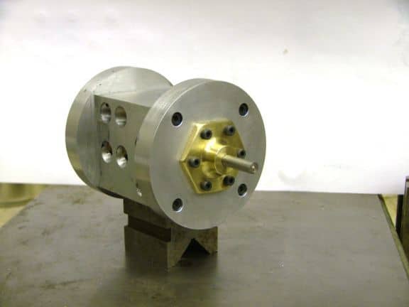 Metal component with central shaft and evenly spaced holes, mounted on a dark gray base with silver finish and black details.