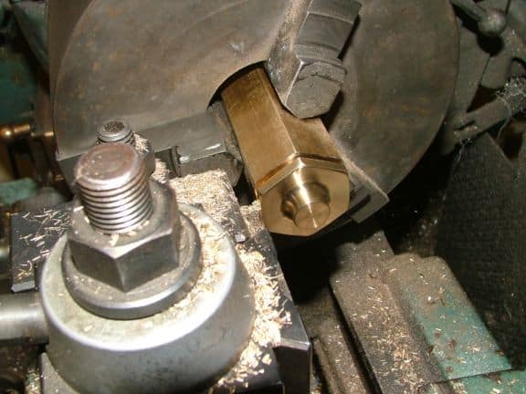 Metalworking lathe with brass piece being machined on bed.