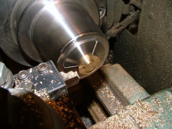 A close-up view of a lathe tool in operation with shavings and a shiny metal surface.