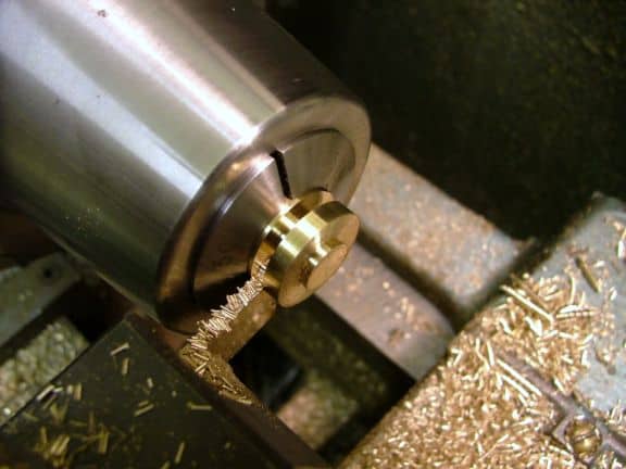 Close-up of a lathe tool shaping brass on a workpiece with a small chip nearby.