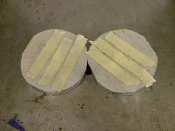 Two rough-textured, circular objects made of concrete or stone with four strips of tape on each surface.