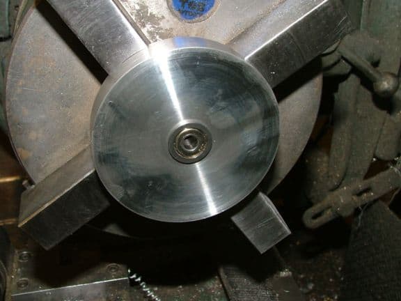 Metal component with circular shape and four radial arms, featuring a blue logo.