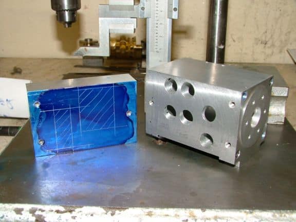 Metal blocks on workbench with tools in background, machine shop setting.