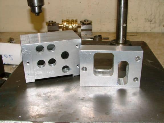 Two aluminum alloy parts on a steel workbench.