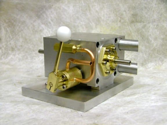 Small metallic device with brass components, white ball, and square base at an angle.