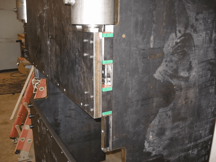 Dark gray metal panel with silver plate secured by green tape on wall or floor in workshop setting.