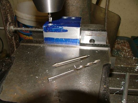 Metalworking lathe or mill with steel worktable and two drill bits on a tool storage bucket in the background.