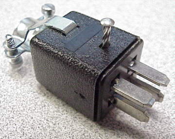 Black electrical connector with two silver prongs on an off-white background and textured surface.